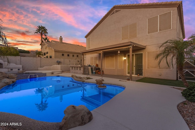 pool at dusk featuring exterior kitchen and a patio