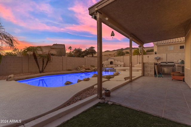 pool at dusk featuring an outdoor kitchen and a patio