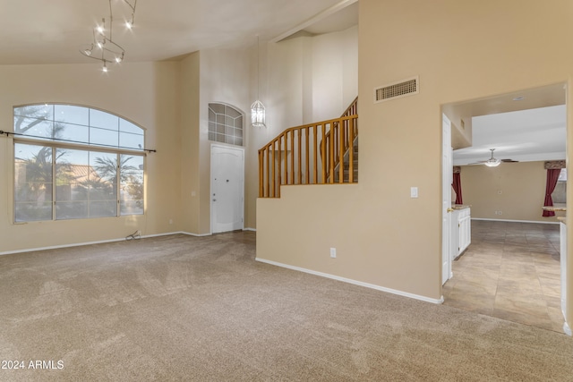 unfurnished living room featuring light carpet, high vaulted ceiling, and ceiling fan with notable chandelier