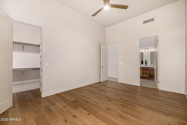 unfurnished bedroom with lofted ceiling, hardwood / wood-style floors, ensuite bathroom, a walk in closet, and a closet