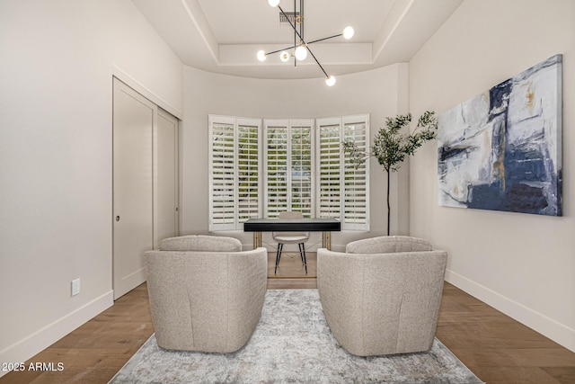 living area with a raised ceiling, hardwood / wood-style floors, and a notable chandelier