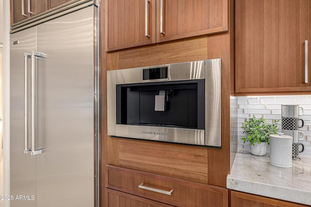 details featuring light stone counters, decorative backsplash, and stainless steel built in fridge