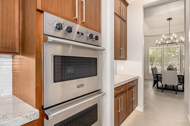 kitchen with pendant lighting, stainless steel double oven, light stone counters, and an inviting chandelier