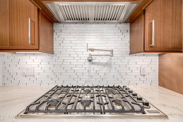 room details with gas stovetop, backsplash, light stone countertops, and exhaust hood