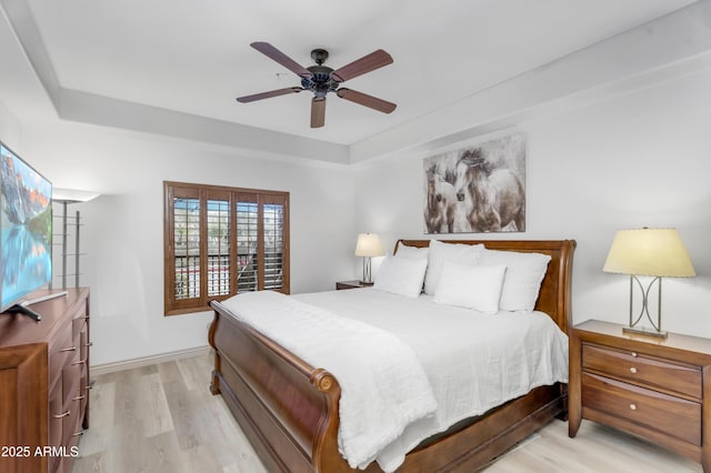 bedroom with ceiling fan, a raised ceiling, and light wood-style flooring