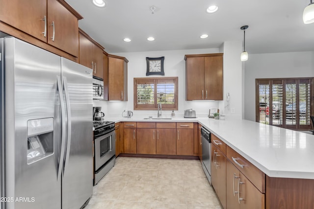 kitchen featuring brown cabinetry, a peninsula, a sink, stainless steel appliances, and light countertops