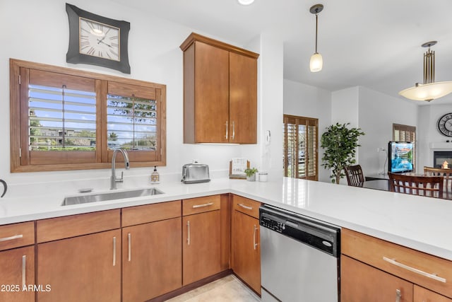 kitchen with brown cabinetry, a sink, hanging light fixtures, light countertops, and stainless steel dishwasher