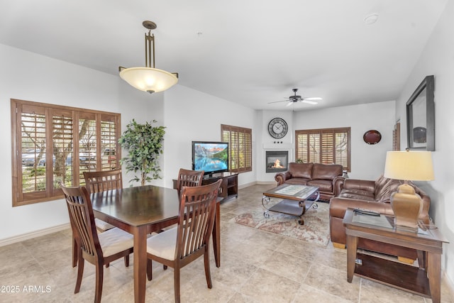 dining room with a glass covered fireplace, a ceiling fan, and baseboards