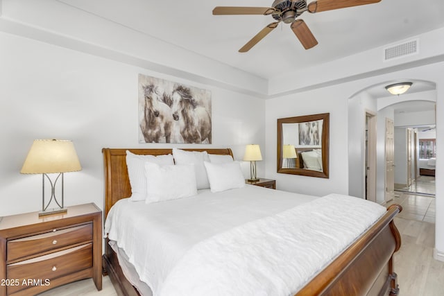 bedroom with arched walkways, visible vents, light wood-type flooring, and ceiling fan