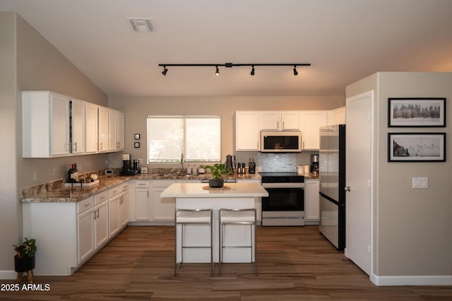 kitchen with appliances with stainless steel finishes, a breakfast bar, white cabinets, a center island, and dark wood-type flooring