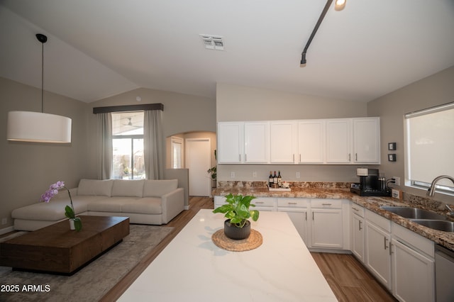 kitchen with vaulted ceiling, pendant lighting, sink, white cabinets, and light hardwood / wood-style flooring