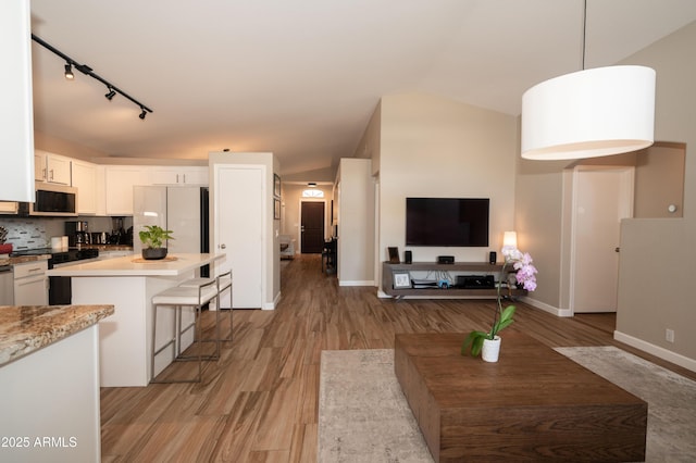 kitchen with backsplash, white cabinets, a kitchen breakfast bar, hanging light fixtures, and light wood-type flooring