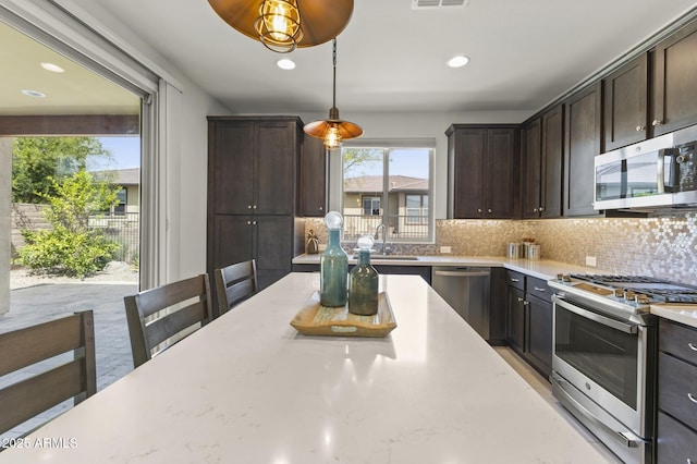 13204 W Via Dona Rd, Peoria, AZ 85383 - kitchen with dark brown cabinets, tasteful backsplash, appliances with stainless steel finishes, a sink, and decorative light fixtures