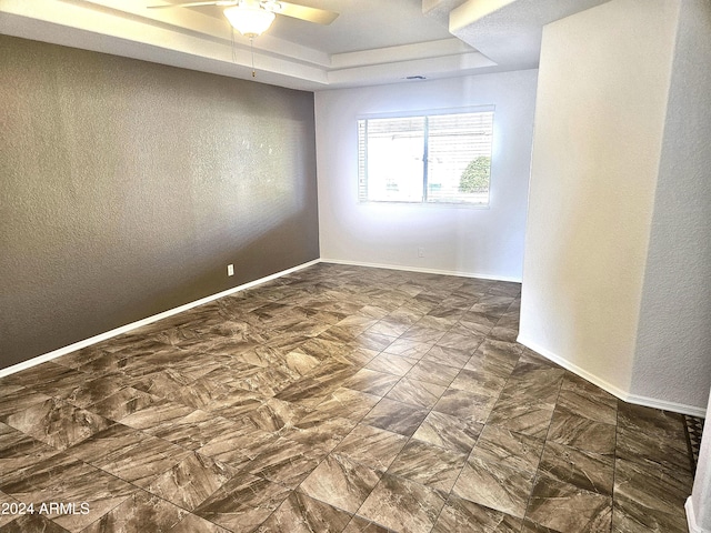 empty room featuring a raised ceiling and ceiling fan