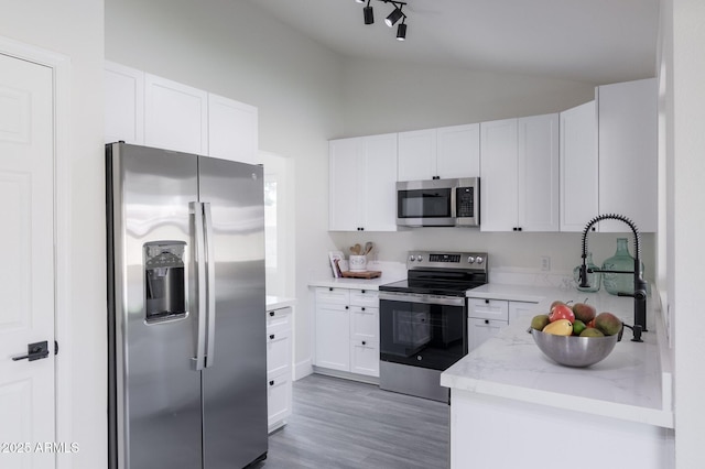 kitchen with light stone countertops, appliances with stainless steel finishes, lofted ceiling, white cabinetry, and sink