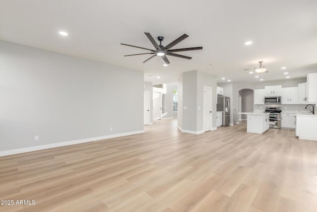 unfurnished living room featuring arched walkways, baseboards, a ceiling fan, and recessed lighting