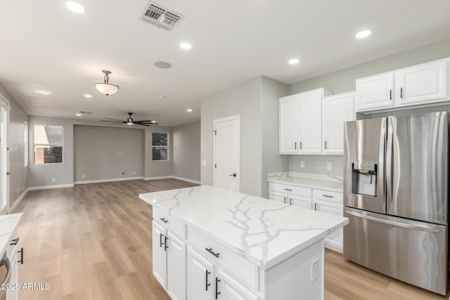 kitchen with visible vents, stainless steel refrigerator with ice dispenser, a center island, light stone counters, and a ceiling fan