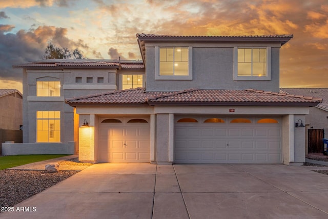 mediterranean / spanish-style home featuring an attached garage, driveway, a tile roof, and stucco siding