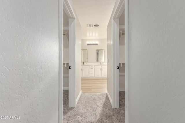 corridor with baseboards, carpet flooring, a textured wall, and visible vents