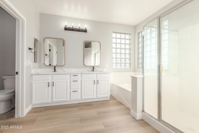 full bathroom with a garden tub, double vanity, wood finished floors, toilet, and a stall shower