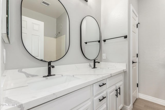 full bath with visible vents, a sink, wood finished floors, and double vanity