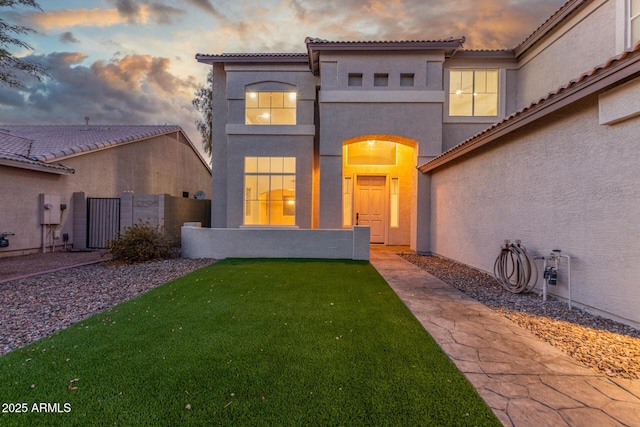 view of front of house featuring fence, stucco siding, a tile roof, and a front lawn