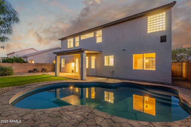 back of house at dusk featuring stucco siding, a fenced backyard, a fenced in pool, a lawn, and a patio