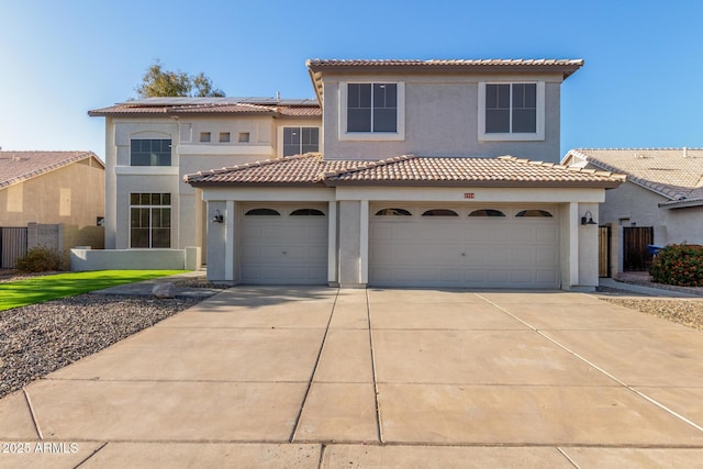 mediterranean / spanish house featuring fence, stucco siding, driveway, a tile roof, and solar panels