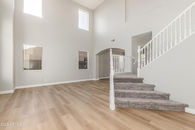 unfurnished living room with arched walkways, high vaulted ceiling, stairs, light wood-type flooring, and visible vents