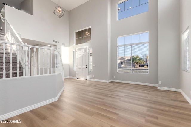 entryway with visible vents, a towering ceiling, wood finished floors, baseboards, and stairs