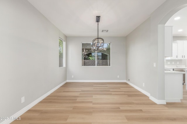 unfurnished dining area with visible vents, arched walkways, light wood-type flooring, baseboards, and a chandelier