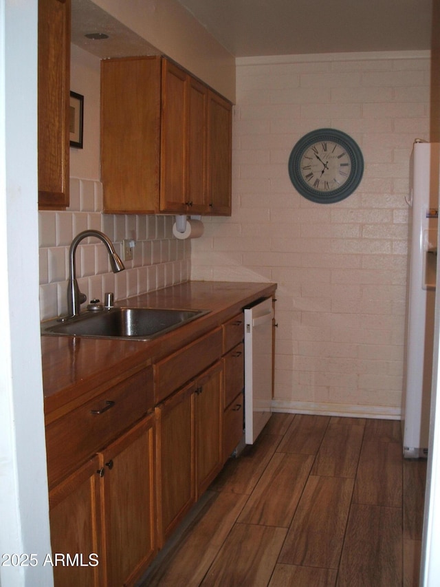 kitchen with sink, white appliances, dark wood-type flooring, backsplash, and brick wall