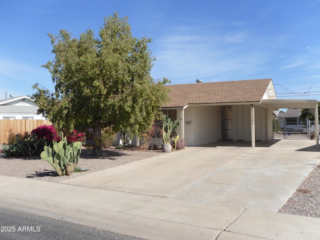 view of front facade with driveway, an attached carport, a shingled roof, and fence