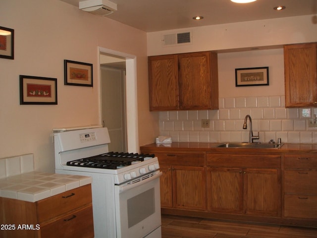 kitchen featuring tile countertops, sink, white gas stove, and backsplash