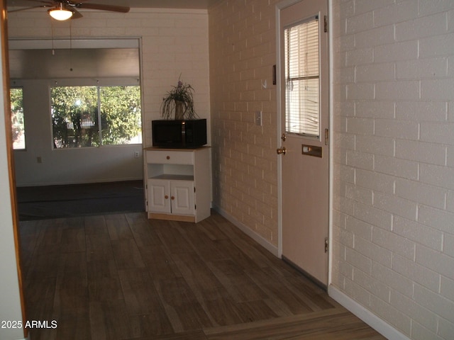 interior space with dark wood-type flooring, ceiling fan, and brick wall