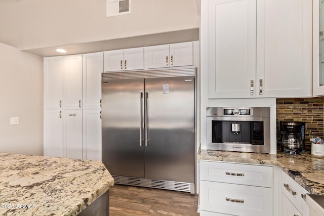kitchen featuring light stone counters, stainless steel appliances, white cabinetry, wood finished floors, and backsplash