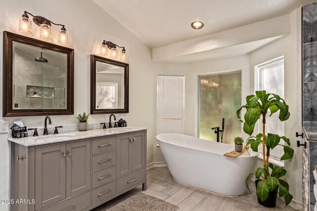 full bath featuring double vanity, baseboards, a freestanding bath, and a sink