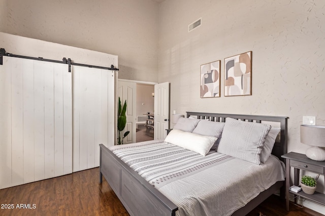 bedroom featuring visible vents, a barn door, a high ceiling, and wood finished floors
