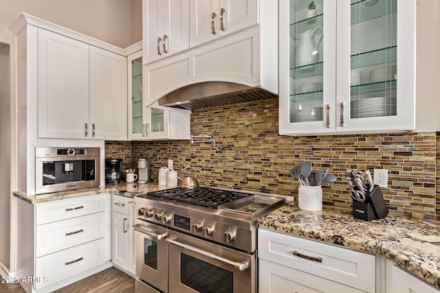 kitchen with glass insert cabinets, white cabinetry, tasteful backsplash, light stone counters, and range with two ovens