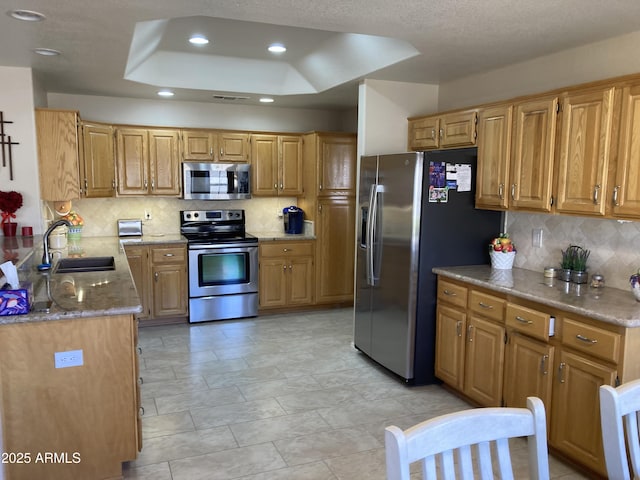 kitchen with sink, backsplash, stainless steel appliances, light stone counters, and a tray ceiling