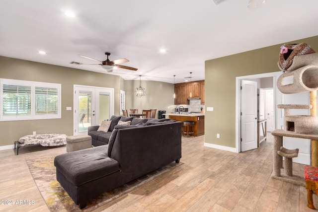 living room featuring ceiling fan with notable chandelier, light wood-type flooring, sink, and french doors