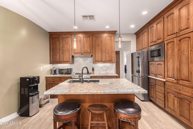 kitchen with light stone counters, stainless steel appliances, sink, decorative light fixtures, and light hardwood / wood-style floors