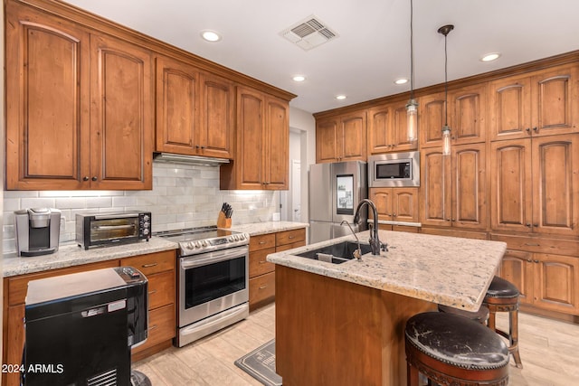 kitchen featuring sink, hanging light fixtures, a kitchen breakfast bar, a center island with sink, and appliances with stainless steel finishes