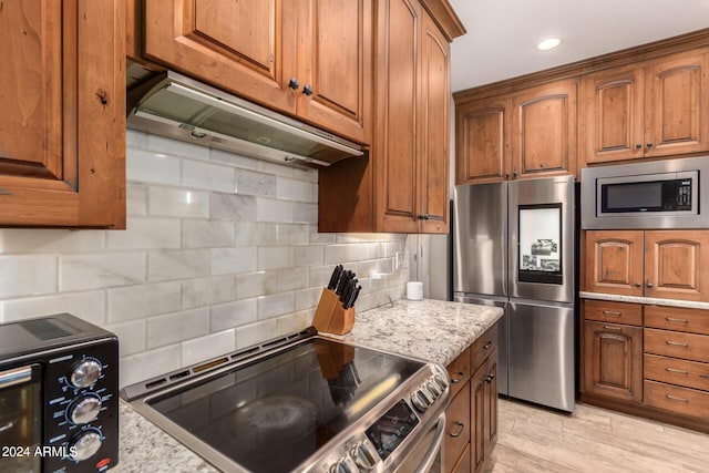 kitchen with light stone countertops, appliances with stainless steel finishes, tasteful backsplash, and light hardwood / wood-style floors