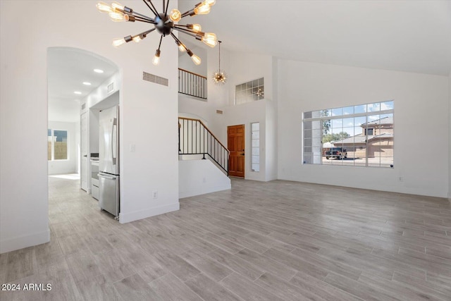 unfurnished living room with light hardwood / wood-style floors, high vaulted ceiling, and a notable chandelier