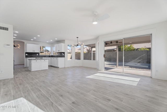 unfurnished living room with ceiling fan with notable chandelier and light hardwood / wood-style floors