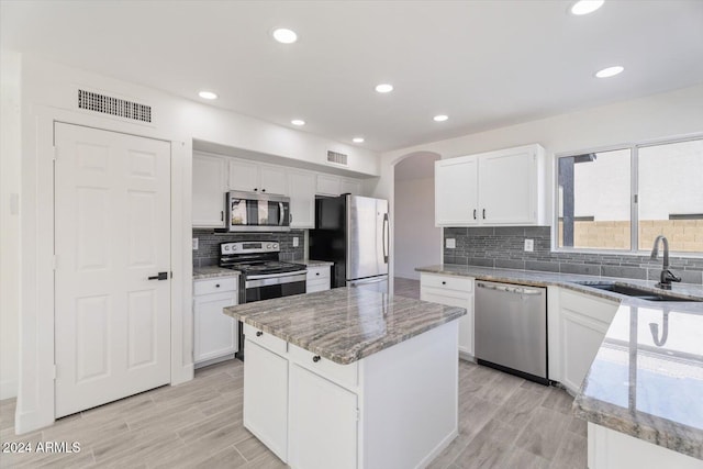 kitchen featuring a center island, white cabinets, sink, appliances with stainless steel finishes, and light stone counters