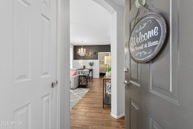 entrance foyer with arched walkways, a notable chandelier, and wood finished floors