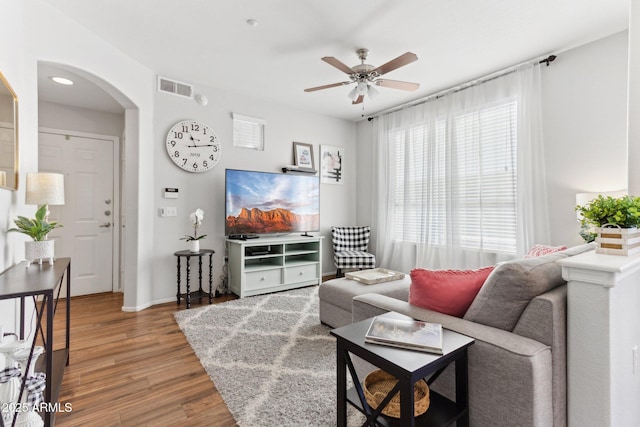 living room featuring visible vents, baseboards, wood finished floors, arched walkways, and a ceiling fan