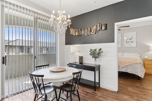 dining room featuring a textured wall, a wainscoted wall, an inviting chandelier, and wood finished floors